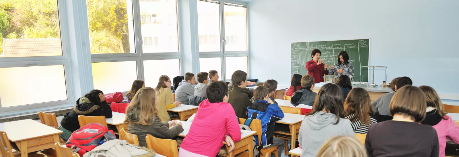 Foto eines Klassenraums mit Schülern und Lehrer vor Schultafel